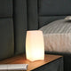 Akku LED-Tischlampe Stele mit App-Steuerung auf einem Nachttisch, warmes Licht, modernes Design.
