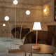 Akku LED-Tischleuchte Lola auf einem Tisch, umgeben von stilvollen Sitzgelegenheiten in elegantem Ambiente.