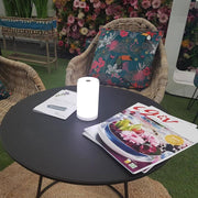 Lampe de table à batterie LED Tub USB-C avec commande par application sur une table avec des magazines et des coussins en arrière-plan.