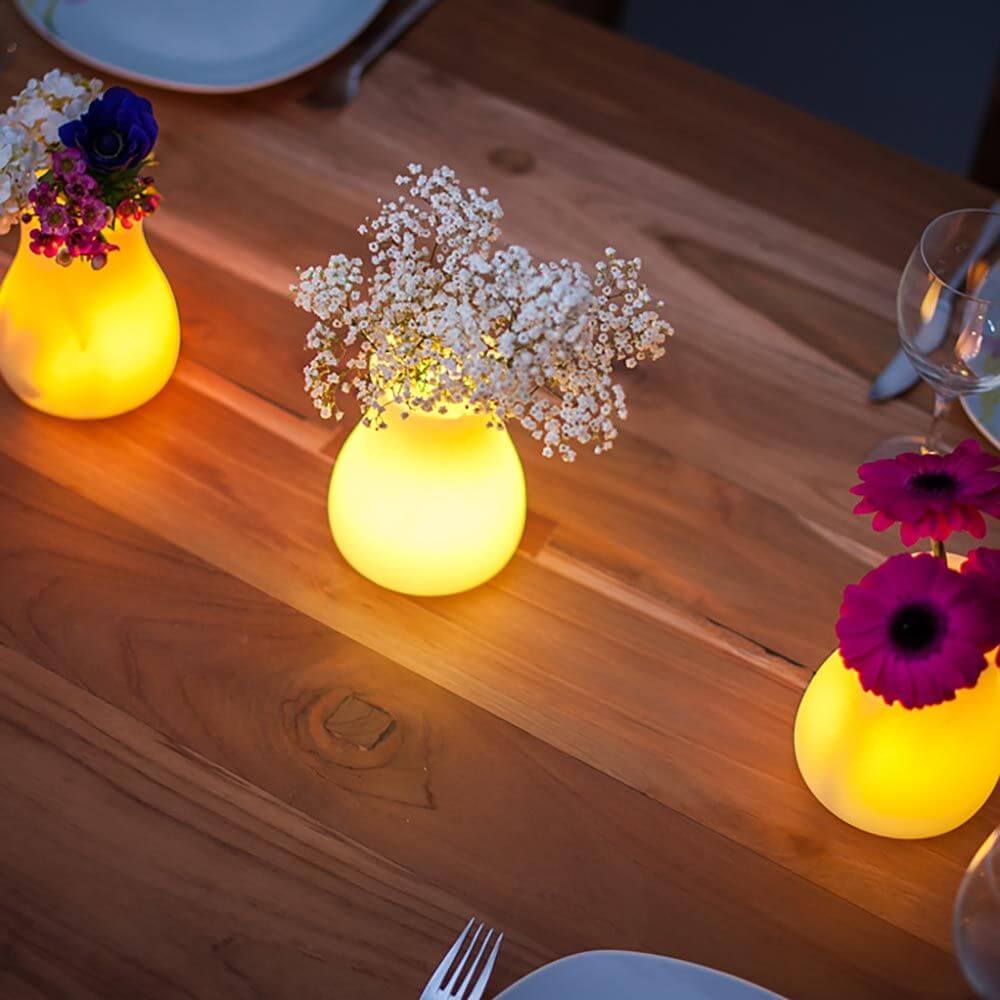 Akku LED-Tischvase Olio mit App-Steuerung auf Holztisch mit Blumendekoration und sanftem Licht.