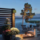Amalfi LED Außen-Wandleuchte in Oliv, elegant illuminiert Terrasse mit Blumen und Blick auf See bei Dämmerung.