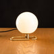 Artemide NH 1217 Tischlampe mit elegantem Messingring und runder Glasleuchte auf Holztisch.