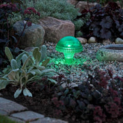Assisi svamp sol LED lampe grøn i et havebed med planter og sten.