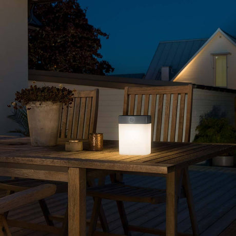 Grey solar LED light Assisi with opal acrylic glass on an outdoor table at night.