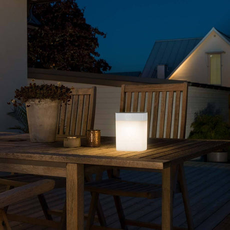 Assisi Solar LED Lamp Wit, opaal acrylglas op een houten tafel buiten bij nacht.