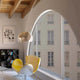Raum mit gelbem und weißem Sessel, modernem Lampendesign und großer Fensterfront mit Blick auf ein Wohngebäude.