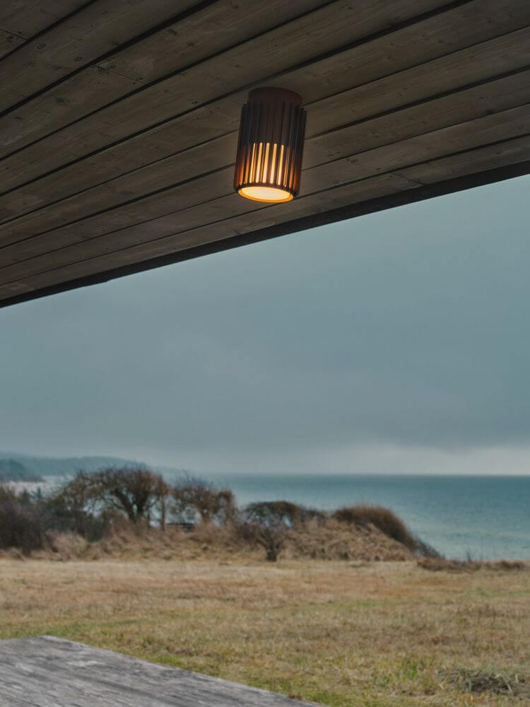Außendeckenlampe Aludra Seaside IP54 an einer Holzdecke mit Blick auf das Meer.