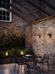 Außenwandlampe Aludra IP54 beleuchtet gemütlichen Außenbereich mit Steinen und Pflanzen.