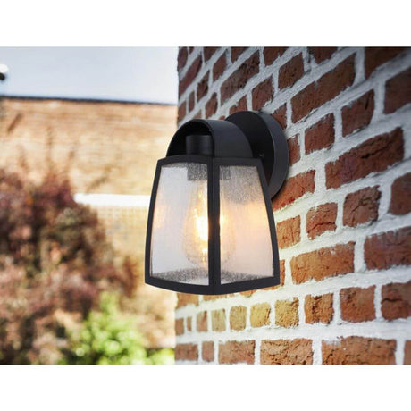 Außenwandlampe Kelsey IP44 Schwarz an einer Ziegelwand mit warmem Licht im Garten.