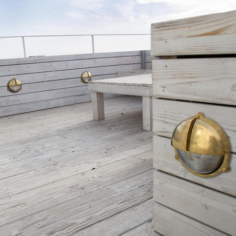 Utendørs vegglampe TIMON IP44 messing maritim installert på en treterrasse, ideell for hagebelysning.