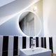 Moderne Badezimmeransicht mit Azos Spiegel Wandleuchte und runder Spiegelfläche.