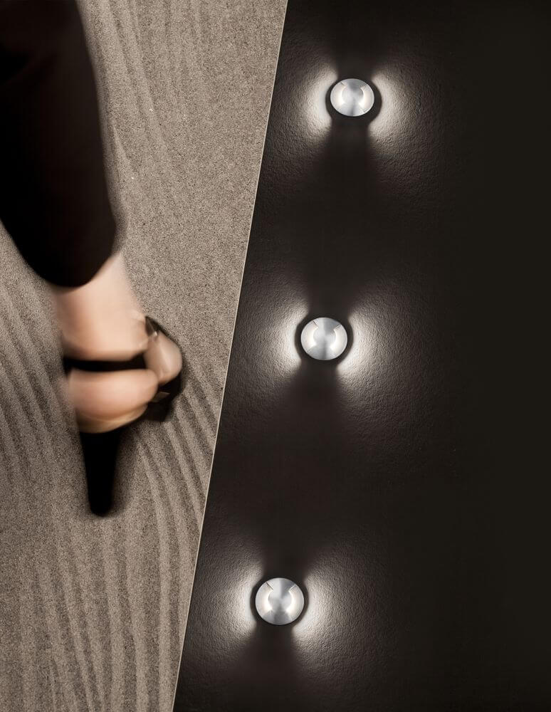 Bang LED Außenbodeneinbauleuchte Nickel IP67 auf einem eleganten Boden mit einem Fuß, der darüber schreitet.