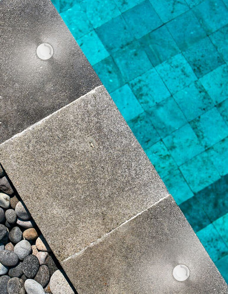 Bang LED outdoor floor recessed light Nickel IP67 in a stylish setting by the pool with decorative gravel.