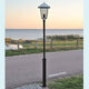Benu Standleuchte galvanisierter Stahl, rauchfarbenes Acrylglas neben einem Radweg am Meer bei Sonnenuntergang.