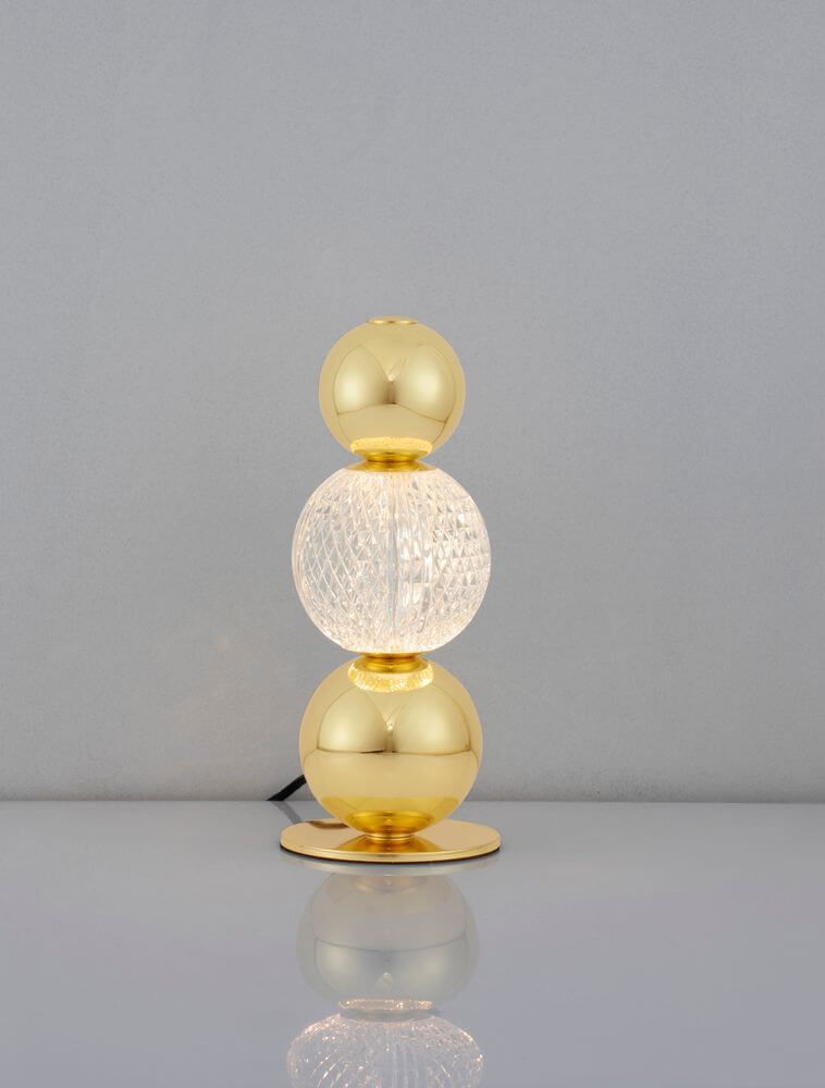 Brille LED Tischleuchte Ø 12cm 3200K Gold auf einem eleganten Tisch vor grauem Hintergrund.