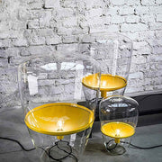 Brokis Stehleuchte Balloons Large in Glas mit gelbem Metallreflektor auf Ziegelwand.