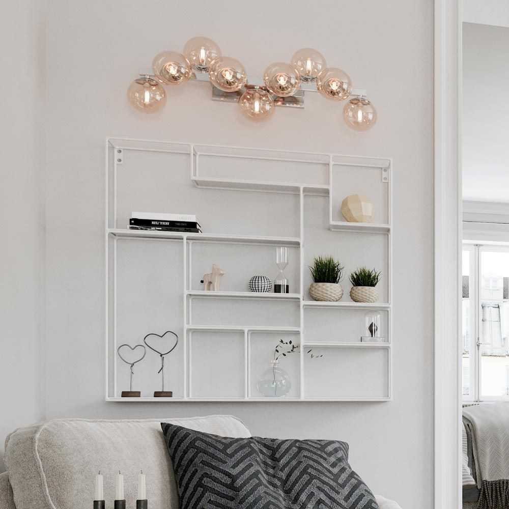 Wandleuchte Splendor 9-flg in Gold und Bernstein, stilvoll über modernem Regal in einem hellen Wohnraum.