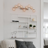 Wandleuchte Splendor 9-flg in Gold und Bernstein, stilvoll über modernem Regal in einem hellen Wohnraum.