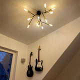 Deckenlampe Heroes 12-flammig Schwarz mit warmem Licht, umgeben von Gitarren an der Wand.