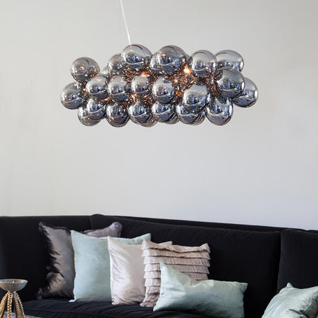 Elegante lampada a sospensione in vetro Gross Bar 80 cm con 38 sfere di vetro posizionata sopra un divano.