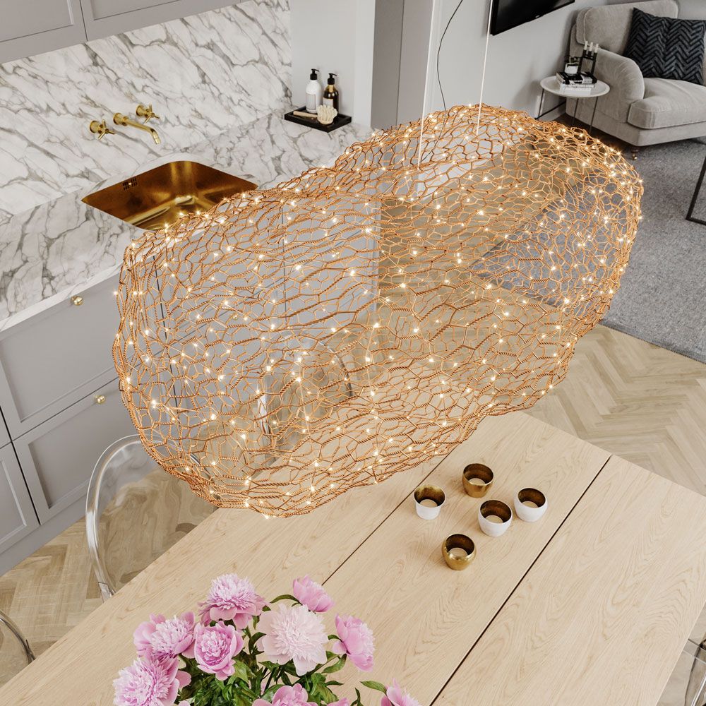 LED-hengelampe Hayden L 76 cm gullfarget over en spiseplass med blomster og moderne interiørdetaljer.