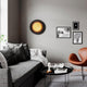 LED-vegglampe Nitra Ø 50 cm svart, gullfarget på grå vegg over en koselig sofa.