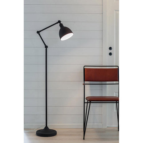 Bazar floor lamp with movable arm in sand black next to a modern chair in a minimalist room.