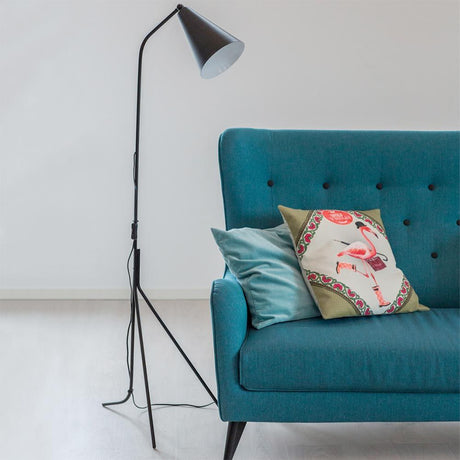 Yukon tripod floor lamp in black next to a blue sofa with cushions in Scandinavian style.