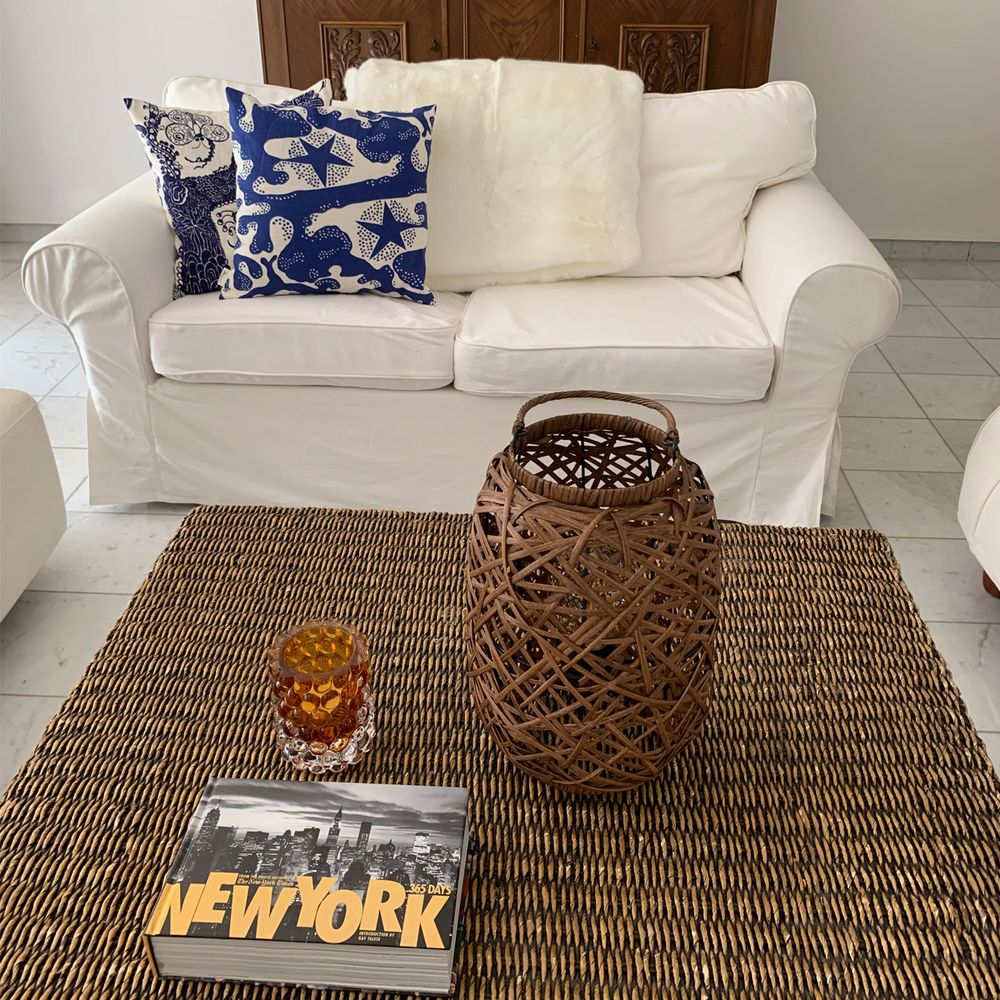Tischlampe Diego aus Rattan auf einem Tisch mit einem Buch und dekorativen Elementen in einem gemütlichen Wohnzimmer.