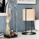 Bordlampe Vieste 45 cm med fløyelsskjerm ved siden av en glasskuppel med dekorative objekter.