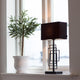 Bordlampe Paragon M svart stoffskjerm ved siden av en plante i vinduet, moderne og kunstnerisk atmosfære.