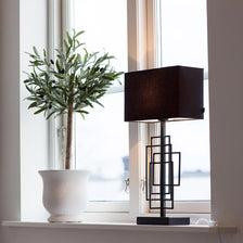 Table lamp Paragon L with black fabric shade beside a plant in the window, stylish room design.