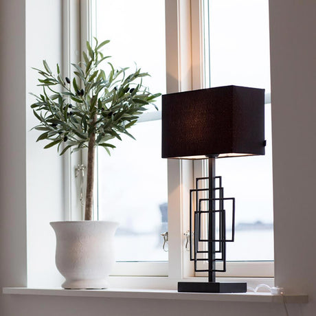 Lampe de table Paragon L avec abat-jour en tissu noir à côté d’une plante dans la fenêtre, design intérieur élégant.