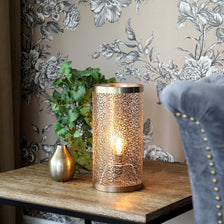Lampe de table Hermine 28 cm laiton sur une table avec un décor floral en arrière-plan.