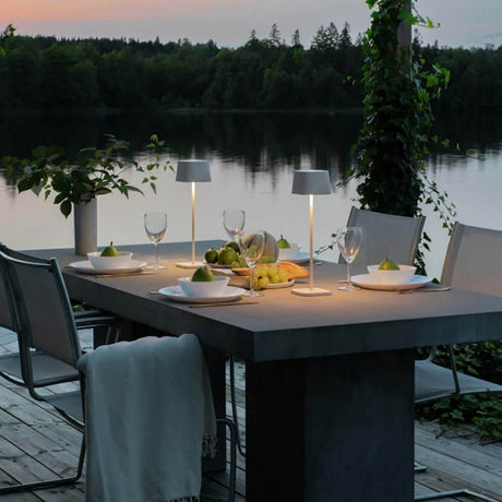Capri USB-Tischleuchte IP54 auf einem Tisch am See bei Dämmerung mit gedecktem Tisch.