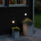 Chieri LED Außenwandlampe IP54 montiert an der Wand, mit Pflanzen in modernen Töpfen im Außenbereich.