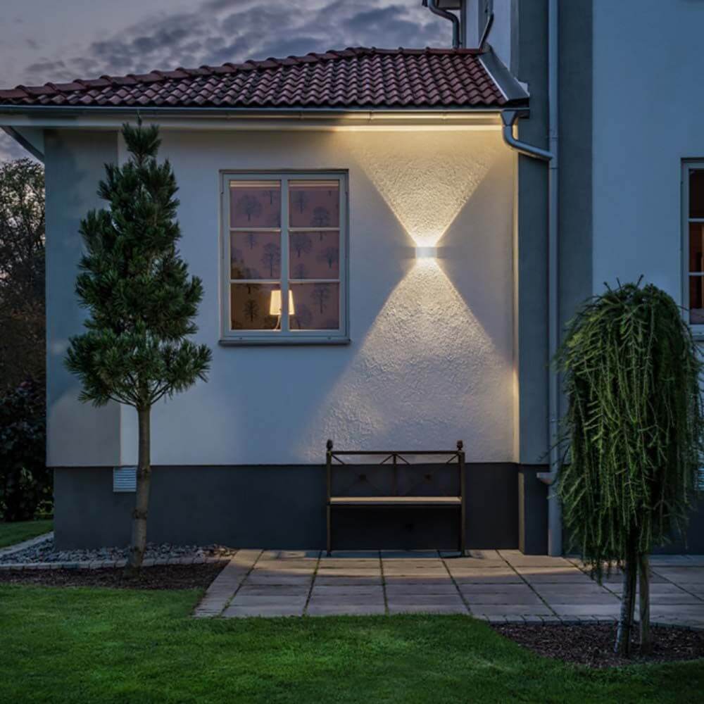 Chieri LED Außenwandleuchte an der Wand eines Hauses mit sitzender Bank und Pflanzen im Außenbereich.