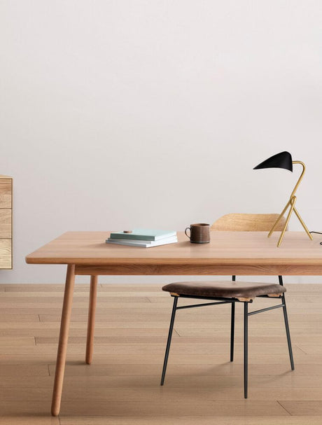 Lampe de table Cork noire et dorée sur un bureau en bois avec chaise et objets décoratifs.