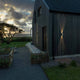Cremona LED Messing Wandleuchte an einer modernen Holzfassade bei Dämmerung.