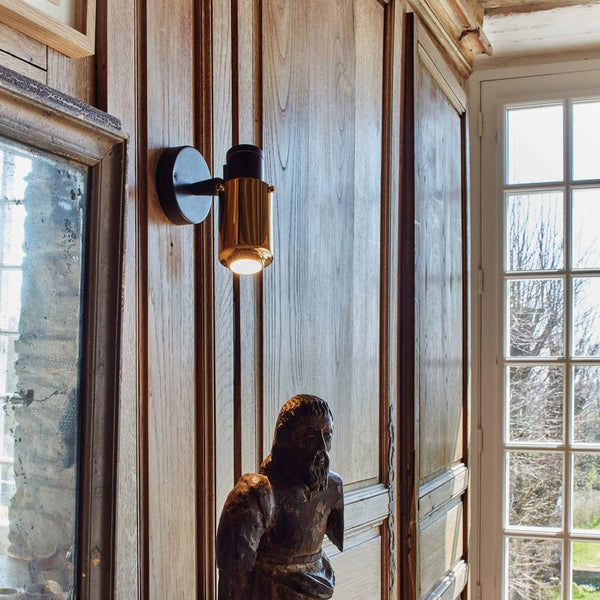 DCWéditions Biny Spot Wandleuchte verstellbar an Holzwand mit Statue im Vordergrund.