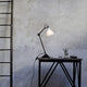 DCWéditions Gras N°205 Tischlampe mit schwenkbarem Schirm auf einem modernen Tisch.