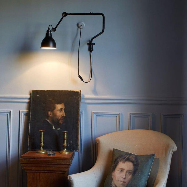 DCWéditions Gras N°303 Wandlampe mit Ausleger in stilvollem Wohnzimmer, beleuchtet ein Porträt und eine gemütliche Sitzecke.