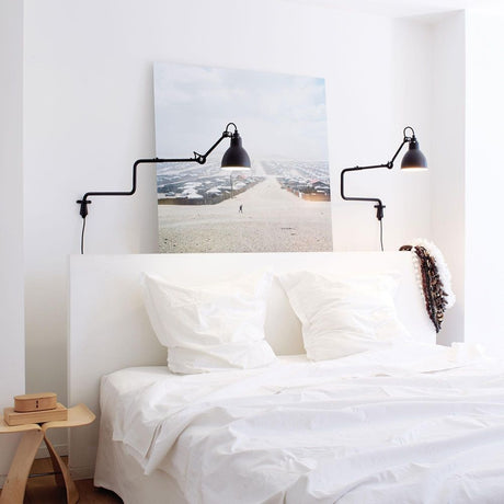 DCWéditions Gras N°303 Wandlampe mit Ausleger über einem Bett mit Kissen und Kunstwerk an der Wand