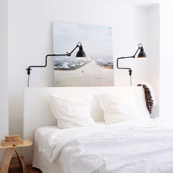 DCWéditions Gras N°303 Wandlampe mit Ausleger über einem Bett mit Kissen und Kunstwerk an der Wand