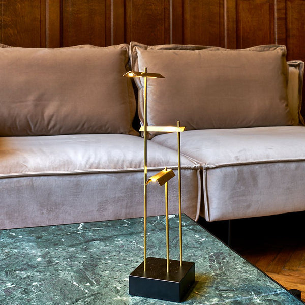DCWéditions Knokke LED lampe de table à аккумуляteur noire et dorée sur une table en marbre vert à côté d’un canapé gris.