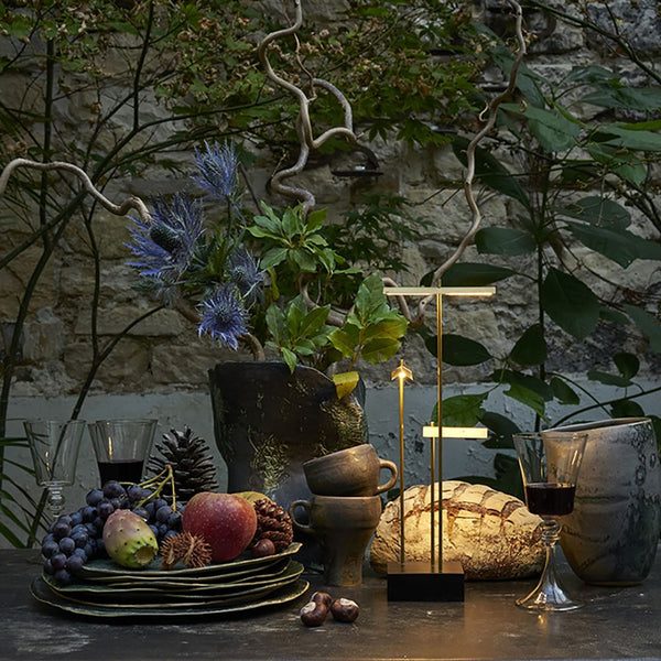 DCWéditions Knokke LED lampe de table à аккумуляteur noire et dorée sur une table avec des fruits et des plantes