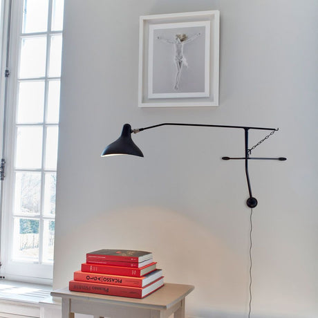 DCWéditions Mantis BS2 Mini LED an einer Wand, umgeben von Büchern und Kunstwerk.