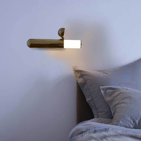 DCWéditions ISP LED-vegglampe i messing plassert på en vegg ved siden av en seng