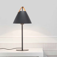 Lampe de table Strap noire avec abat-jour noir et poignée en cuir sur une table.