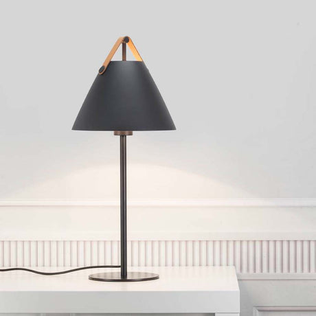 Tischlampe Strap Schwarz mit schwarzem Lampenschirm und Ledergriff auf einem Tisch.